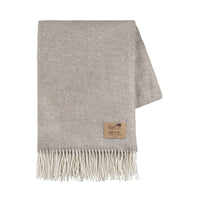 The Juno Cashmere Throw by Lands Downunder is a folded light grey luxury wool blanket with a subtle herringbone pattern, cream fringed edges, and a brown leather patch label in one corner.