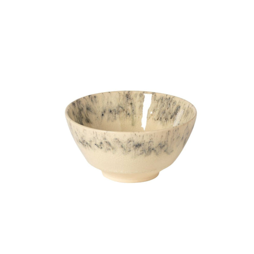 The Costa Nova Madeira Dinnerware Cream bowl features handcrafted Portuguese stoneware with a cream base and dark speckles around its upper half, displayed against a plain white background.