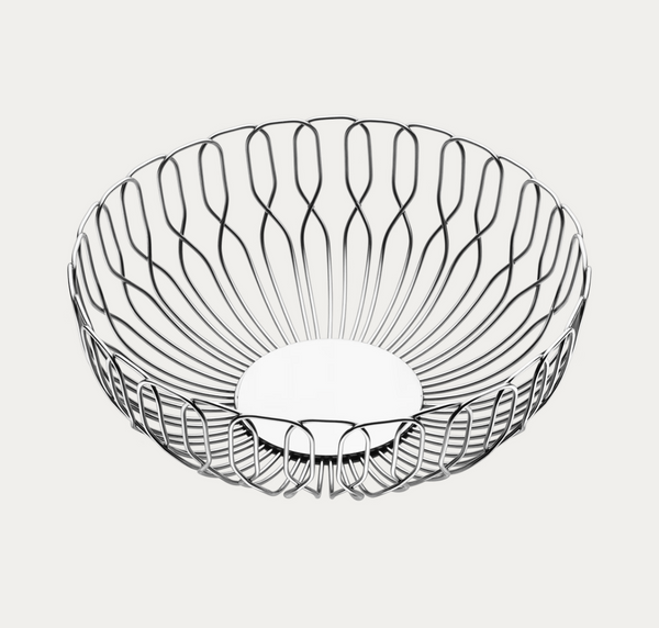 The Alfredo Bread Basket - Small by Georg Jensen is a round, open wire basket with a curved, sculptural design and a flat base, crafted from shiny stainless steel. Shown against a plain white background, this stylish piece is perfect for serving bread or fruit and adds a modern touch to any table setting.