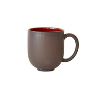 The Tourron Dinnerware Cerise ceramic mug by Jars - Rosenthal features a matte dark brown exterior, glossy red interior, round shape, and large handle. Dishwasher safe, it’s shown on a plain white background.