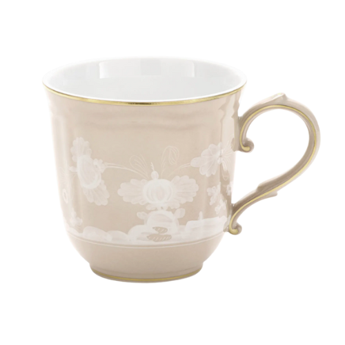The Ginori 1735 Oriente Italiano Beige Meringa is a tan porcelain mug with white floral detailing, gold rim, and handle.