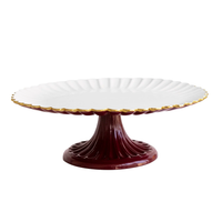 Beatriz Ball Encanto Vienna Pedestal Cake Plate - Bordeaux & White, a handcrafted aluminum plate with a white, scalloped-edge top trimmed in gold and a deep red fluted base.