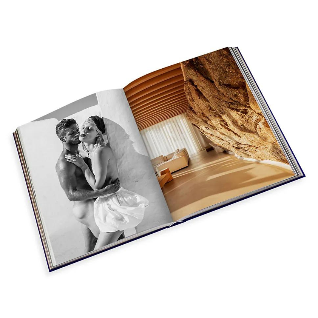 The Assouline "Travel Series - Mykonos Muse" book is open, showing a black-and-white couple’s embrace on the left page and a vivid photo of a sunny modern interior on the right, capturing the elegance of a luxury beach escape.