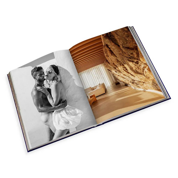 The Assouline "Travel Series - Mykonos Muse" book is open, showing a black-and-white couple’s embrace on the left page and a vivid photo of a sunny modern interior on the right, capturing the elegance of a luxury beach escape.