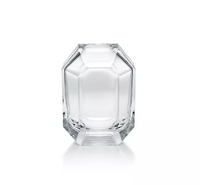 The Baccarat Octogone Bud Vase features clear, faceted glass with sharp edges and smooth surfaces, standing elegantly on a white background and reflecting the refined style of Baccarat chandeliers.