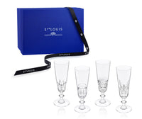 Four clear crystal Saint-Louis/Hermes Queen’s Hall Champagne Flute- Set of 4 glasses with varying etched patterns, displayed next to a blue gift box wrapped with a branded ribbon.