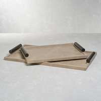 Two rectangular beige trays with raised black cylindrical handles are stacked at an angle on a light grey surface. The Zodax Belle Rectangle Leather Tray set, crafted in luxurious mink leather, seamlessly blends elegance and functionality for all your entertaining needs.