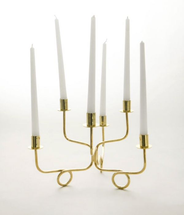 The Together Candelabra - Gold by Byaas features curved arms, a brass finish, and six white taper candles, making it a striking modern centerpiece against a white background.