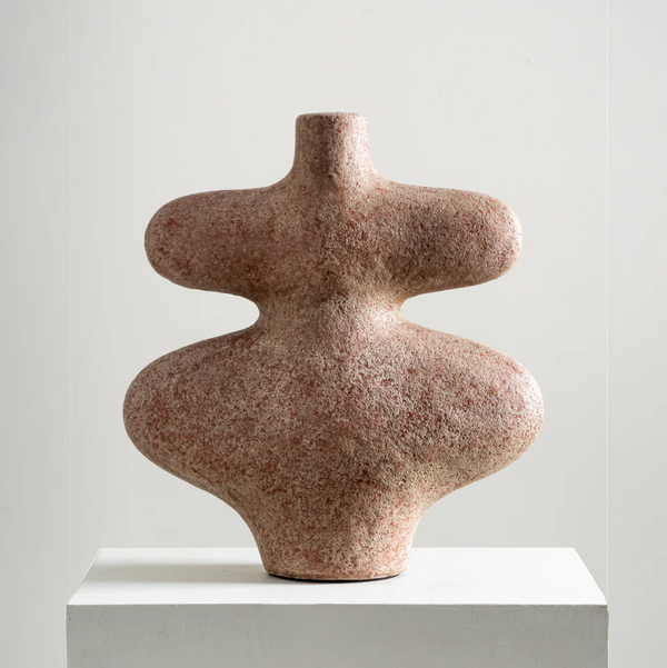 The Oversized Belle by Rumma—an artisanal terracotta vase with a textured, abstract design, narrow neck, and wide rounded midsection—sits on a white pedestal against a plain light background.