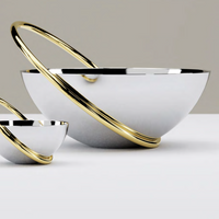 Two Anna New York Ring Fruit Bowls, featuring smooth stainless steel and bold gold rings, sit on a white surface. The different sizes create a modern, minimalist centerpiece perfect for any setting.