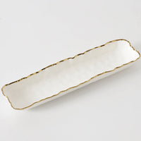 The Portofino Small Tray by PAMPA BAY is a long, rectangular porcelain serving dish with wavy edges and a metallic gold trim—an elegant, oven-safe dinnerware piece shown on a plain white background.