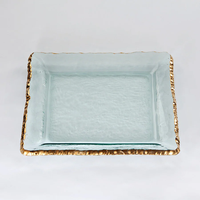 The Annieglass Edgey Square Platter Gold 12" is a handmade, clear glass platter with a slightly textured surface and an uneven 24kt gold rim, shown on a plain white background.