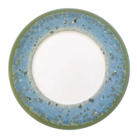 The Nymphea Dinnerware by Jaune De Chrome features a round ceramic plate with a white center, wide blue and green mottled border, olive-green rim, and watercolor-inspired decorative edge reminiscent of Limoges porcelain.
