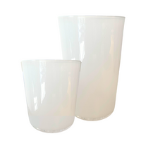 Two translucent white Dynasty Cups Cotton by Gary Bodker of different heights stand side by side on a plain background, showcasing minimalist design and smooth, rounded shapes with elegant reflective surfaces.