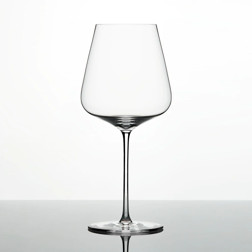 A single Grand Cru Selections / Zalto Bordeaux Glass, featuring a thin stem and wide bowl, is shown against a plain white background with its reflection visible on a glossy surface.