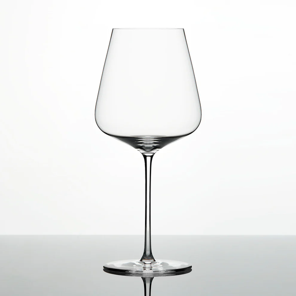 A single Grand Cru Selections / Zalto Bordeaux Glass, featuring a thin stem and wide bowl, is shown against a plain white background with its reflection visible on a glossy surface.