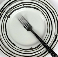 A metal fork rests on a white ceramic Michael Wainwright Linea Dinnerware plate, featuring bold black uneven stripes, stacked atop a matching larger plate with the same striking pattern.