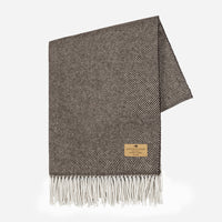 The Juno Cashmere Throw by Lands Downunder features a brown and cream herringbone pattern, white fringes, and a tan stitched label in one corner, shown against a plain white background.