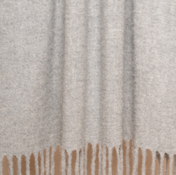 A close-up of the Brushed Boucle Throw by Thread & Butter, featuring a soft, light gray baby alpaca blend with a textured surface, natural sheen, and long fringes hanging from the bottom edge.