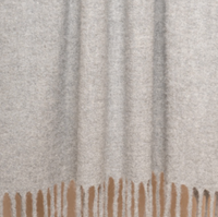 A close-up of the Brushed Boucle Throw by Thread & Butter, featuring a soft, light gray baby alpaca blend with a textured surface, natural sheen, and long fringes hanging from the bottom edge.
