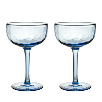 Two Puro Cocktail Coupe S/2 glasses by Juliska, featuring clear blue-tinted, textured bowls and slender stems, stand side by side against a white background—perfect for serving cocktails and elegantly packaged in a gift box.