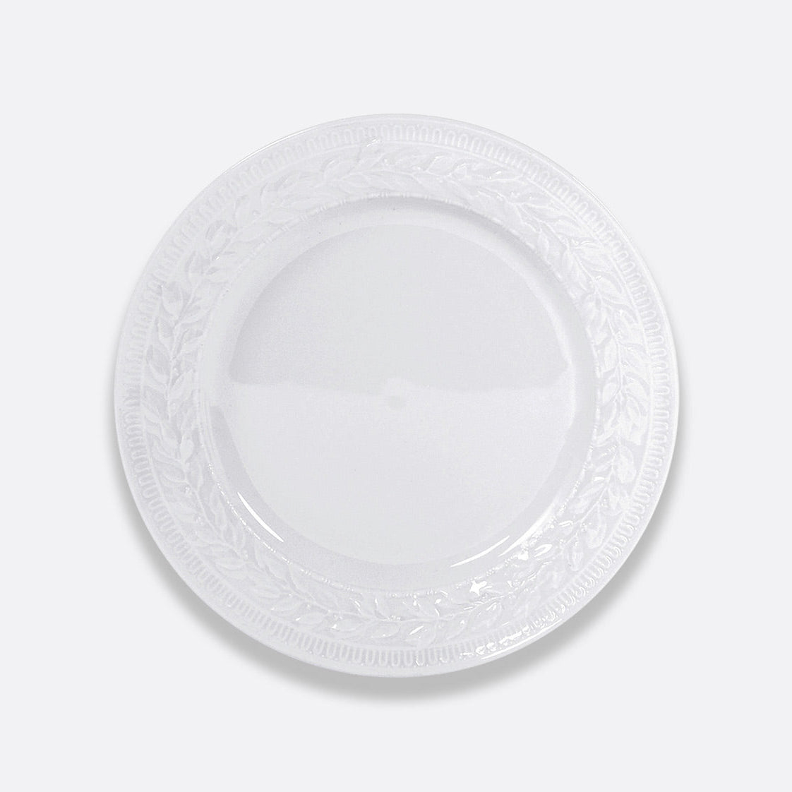 The Bernardaud Louvre Dinnerware features a white plate with a raised embossed laurel leaf pattern around the rim, inspired by Renaissance motifs and French architecture.
