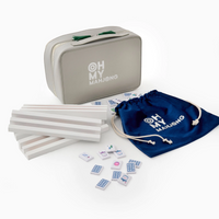 The Oh My Mahjong Mahjong Debutante Travel Tile Set includes a gray carrying case with the brand's logo, white tile racks, a blue drawstring pouch, and mahjong tiles—perfect for gaming on the go.
