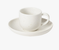 A Pacifica Salt Dinnerware cup with handle sits on its matching saucer, both by Casafina/Costa Nova. Made of white stoneware, they feature a simple design with subtle speckles and a matte finish against a plain white background.