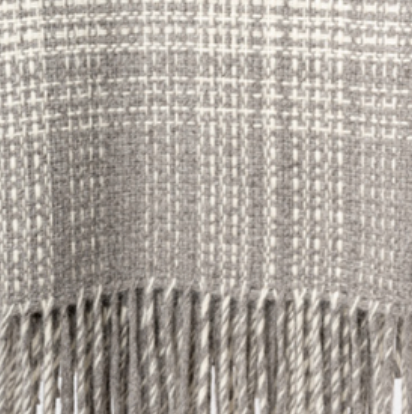 A close-up of the Rustic Alpaca Plaid Throw by Thread & Butter, featuring a beige and white plaid pattern, long twisted fringe, and expertly woven in Peru from luxurious alpaca fibre.