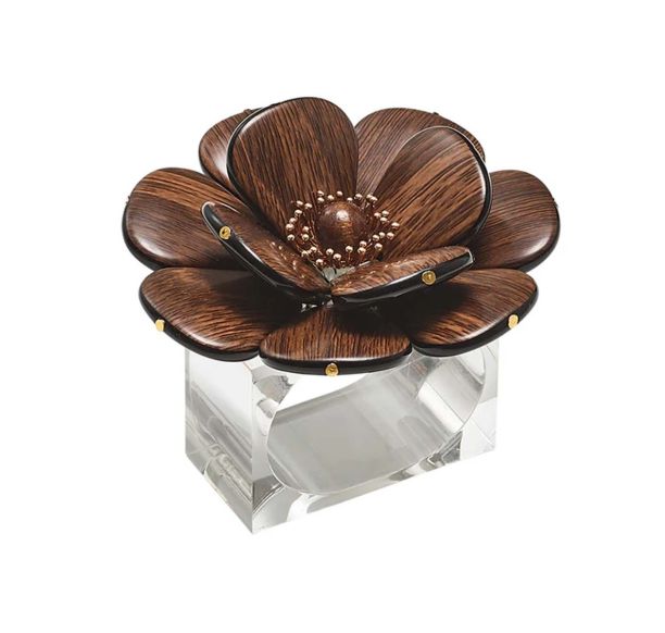The Kim Seybert Begonia Napkin Rings Set of 4 features large dark brown flowers with petal and bead accents atop a clear rectangular base, adding a decorative touch to any table setting.