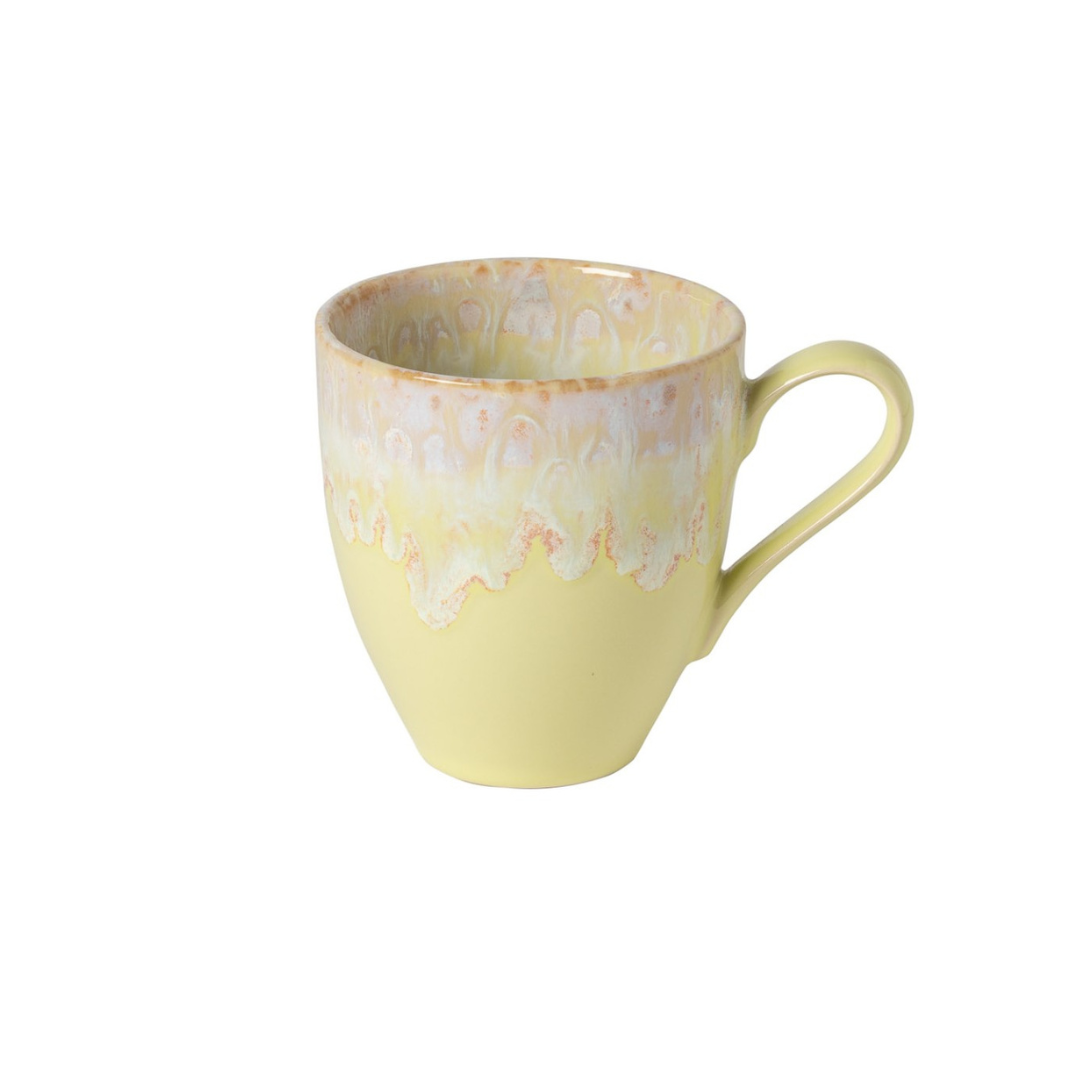 The Costa Nova Taoromina Dinnerware Yellow mug features a curved handle and a decorative rim with a light beige and off-white textured glaze, showcasing artisanal craftsmanship. It is photographed against a plain white background.