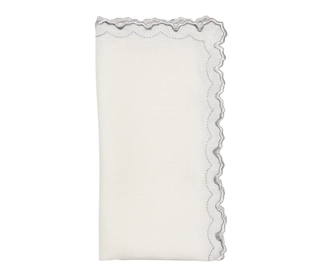 The Arches Napkin Set of 4 by Kim Seybert features folded white linen napkins with one scalloped, embroidered edge in wavy gray stitching, shown against a plain white background.