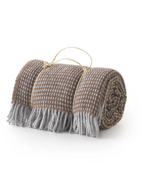 A Soft Idea's Uniwaffle Throw, a brown and gray waffle-textured blanket with fringed edges and a string handle, is shown rolled up on a white background.