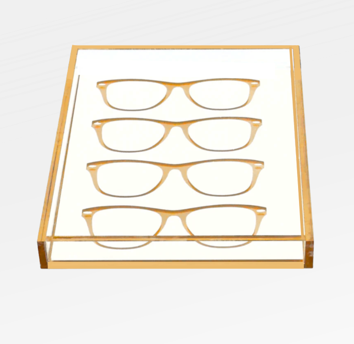The Eye Candy Specs Eyeglass Tray is a clear luxury tray with a gold border, elegantly displaying four pairs of eyeglass frames in two neat rows on a white background.