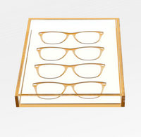 The Eye Candy Specs Eyeglass Tray is a clear luxury tray with a gold border, elegantly displaying four pairs of eyeglass frames in two neat rows on a white background.