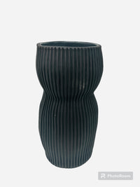 The Curvy Round Vase Black by CYM Warkov Ceramics features a tall, curvy hourglass shape, ribbed vertical grooves, and a dark gray ceramic finish. This limited edition artisan piece stands out against a plain white background.