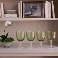 Four green, swirl-patterned Beatriz Ball GLASS French Swirl All Purpose glasses sit on a shelf next to a potted white orchid.