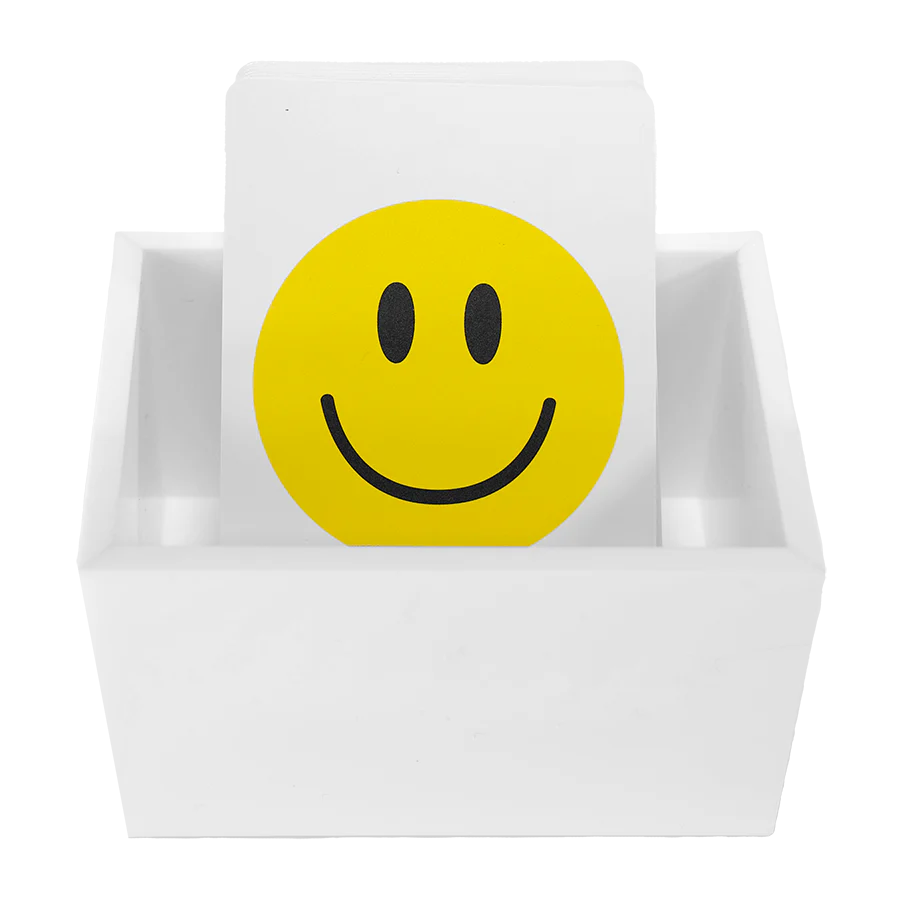 The Canasta Sets Canasta 2 Deck Holder is a white card holder displaying cards, with the front card showing a bold yellow smiley face—ideal for organizing or enhancing your Canasta card games.