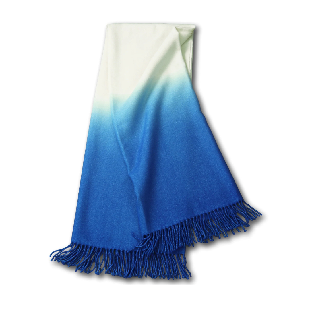 The Johanna Howard Dip Dye Throw features a soft ombré design fading from white to deep blue, finished with blue fringed tassels along the edge.