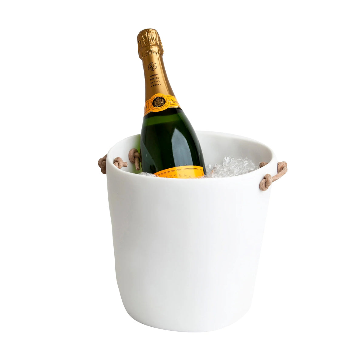 A bottle of champagne rests in a Tina Frey Champagne Bucket Leather Handle, surrounded by ice cubes, set against a plain white background.