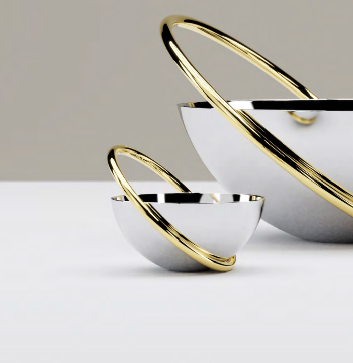 Two reflective stainless steel Anna New York Ring Nut Bowls rest on a white surface, each surrounded by intersecting gold rings. Their modern, sculptural design makes them ideal for luxury home décor.