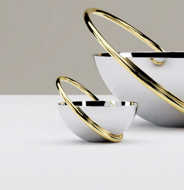 Two reflective stainless steel Anna New York Ring Nut Bowls rest on a white surface, each surrounded by intersecting gold rings. Their modern, sculptural design makes them ideal for luxury home décor.