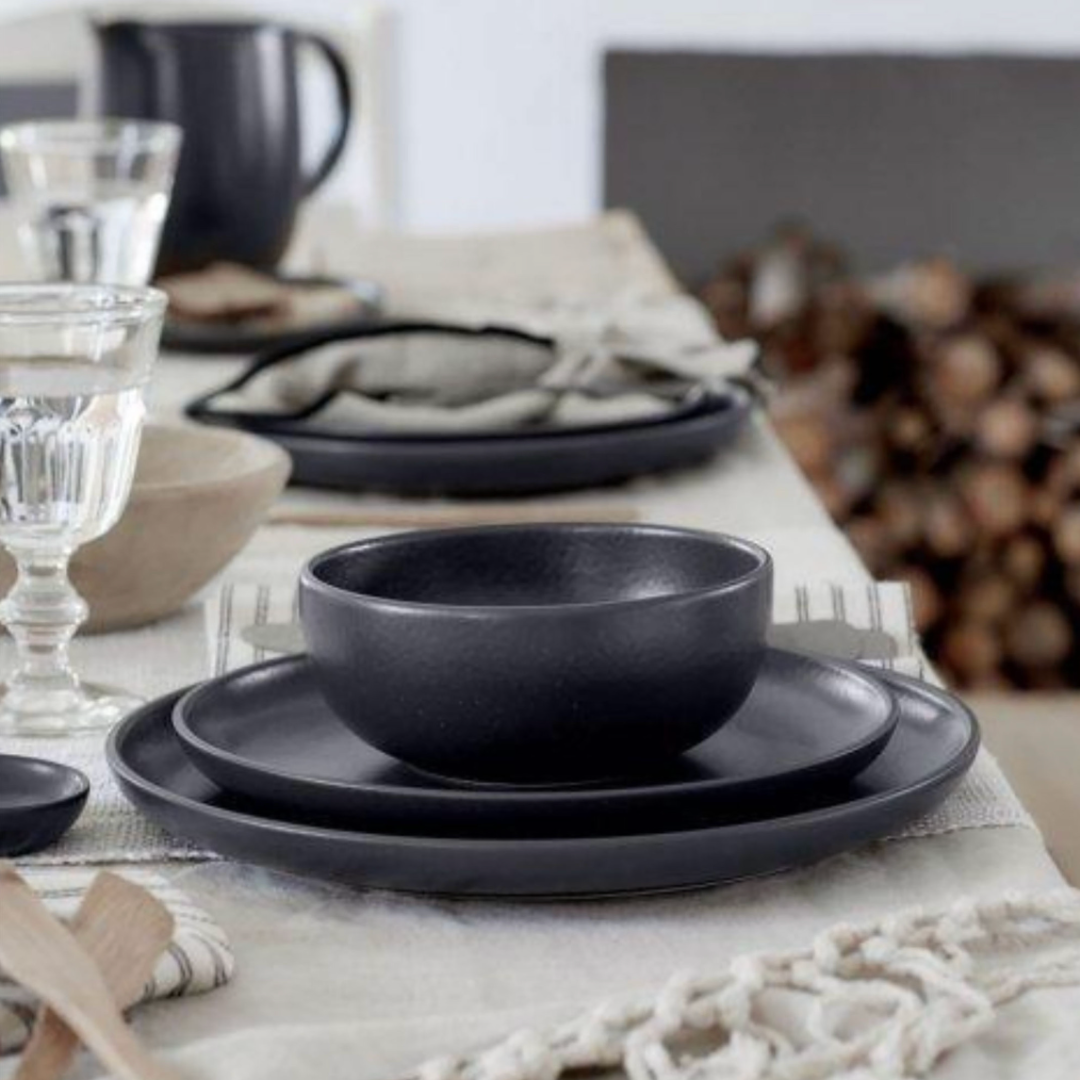 The Casafina Pacifica Dinnerware Grey set, featuring plates and bowls, is arranged on a textured linen tablecloth. Both dishwasher and microwave safe for convenient everyday use.