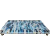 The Eye Candy Raised Serving Board Paint Stroke Blue features a rectangular blue design with white and yellow brushstroke accents, elevated by four metal corner feet.