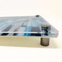 Close-up of the Eye Candy Raised Serving Board Paint Stroke Blue, a rectangular acrylic board featuring a blue abstract design, mounted on metal standoffs that accentuate its thickness and elevated position against a white background.