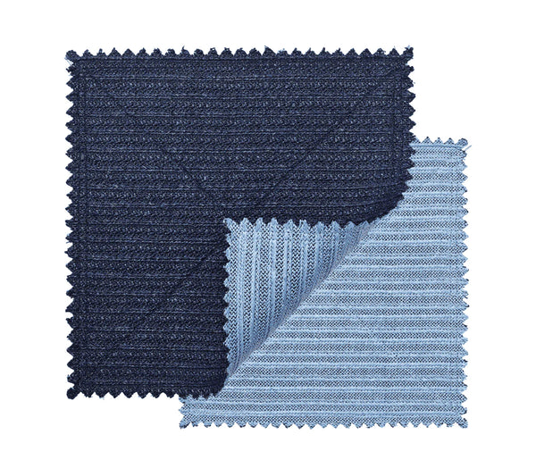 The Kim Seybert Vista Reversible Placemat s/4 in Navy & Periwinkle features two square, ribbed-textured placemats with zigzag edges; the navy piece overlaps the periwinkle one, whose corner is folded to show both reversible sides.