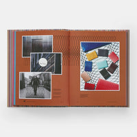 An open Paul Smith book by Phaidon/Hachette features a rust-red spread with black geometric lines and black-and-white British fashion photos on the left, while colorful wallets are displayed on a patterned surface to the right.