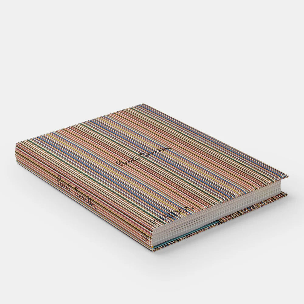 A closed hardcover book titled "Paul Smith" from Phaidon/Hachette, featuring a colorful striped cover and cursive Paul Smith text on the front and spine, is shown resting on a plain white surface.