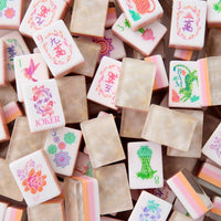 A vibrant pile of Oh My Mahjong’s Pearlescent Mahjong Tiles Set showcases colorful tiles with intricate designs, numbers, and symbols. Accented in pink, green, and orange hues, some tiles feature flowers, birds, or the word JOKER—evoking the lively charm of a floral mahjong set.
