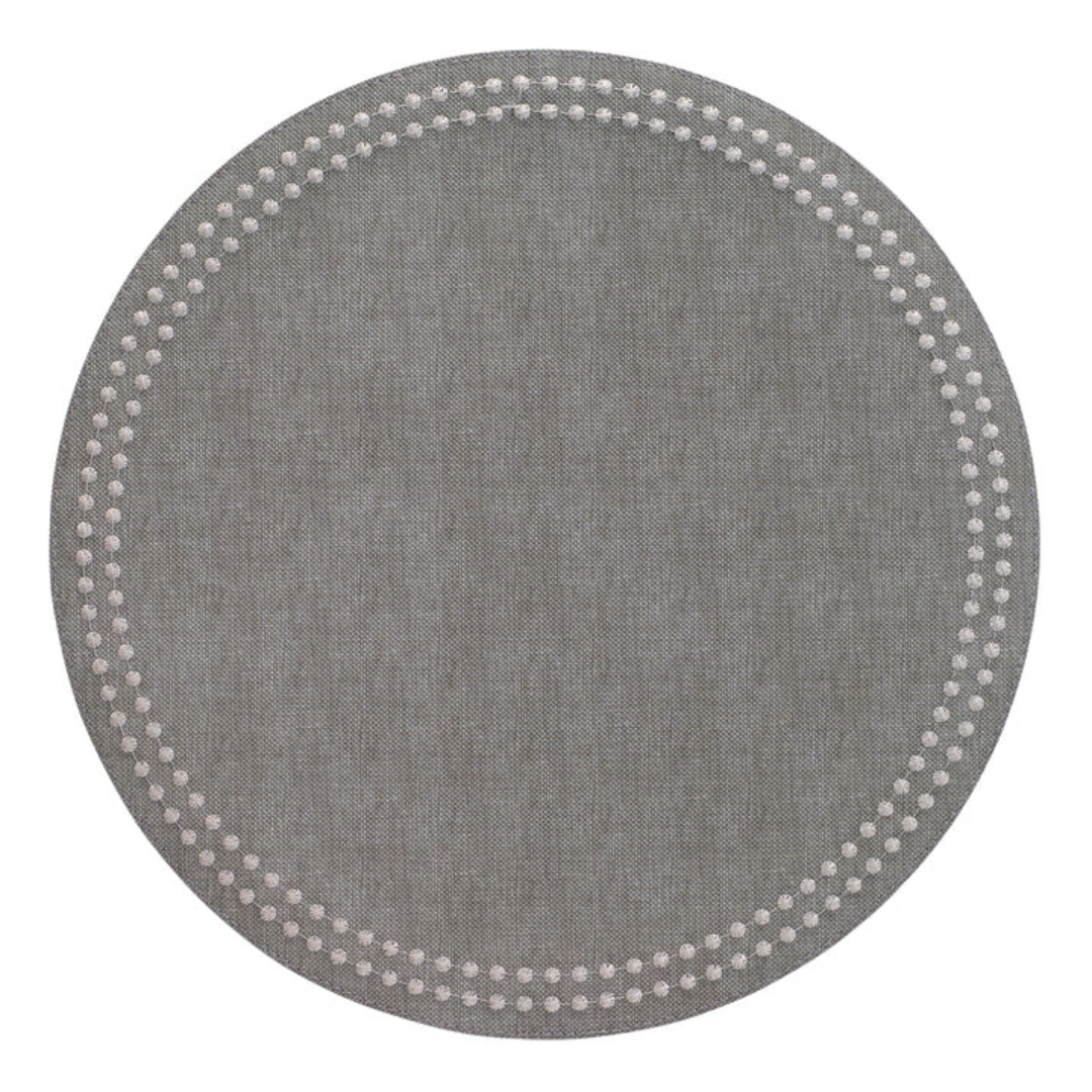 The Bodrum Pearls Round Placemat Set of 4 in gray is made from phthalate-free vinyl and features a subtle fabric texture with small white dots forming two concentric circles near the edge.